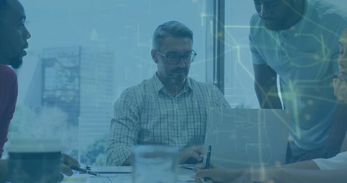 Leaning man with glasses and checked shirt typing and pointing at meeting table, laptop papers pens