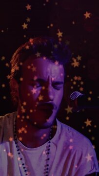 Performing man reacting to light cue, singing and striking stick by mic, wearing beads under stars
