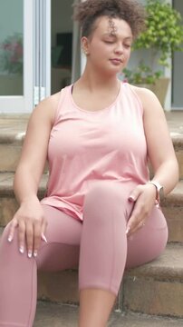 Vertical video: Preparing to leave woman in pink tank tying sneakers on steps, checking smartwatch