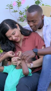 Vertical video: Tickling father leaning in and mother cuddling child on steps for playful bonding