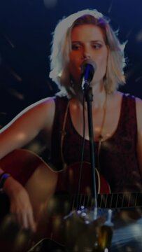 Camera focusing, female singer in sleeveless top strumming acoustic guitar, singing for club, glass
