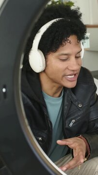 African American man prompted by pink phone with ring light, speaking, glancing, gesturing, filming