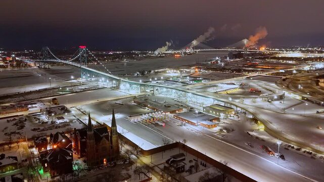 Ambassador Bridge crossing Detroit River with customs plaza and city lights under winter snow, Detroit, Michigan