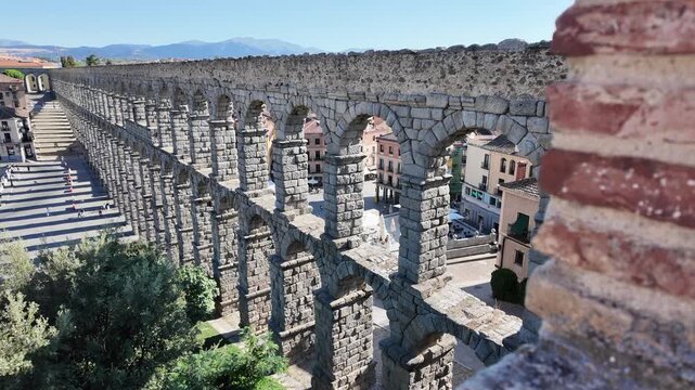 Wide aerial view of Segovia aqueduct stretching across city with repeating arches under bright blue sky.