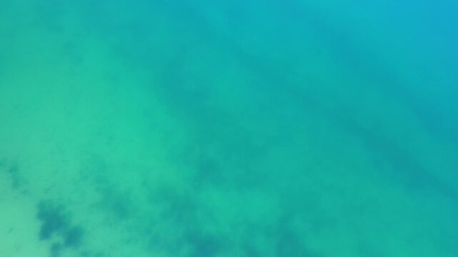 Top-down view of turquoise alpine water with submerged patterns and icy tones visible beneath the lake surface