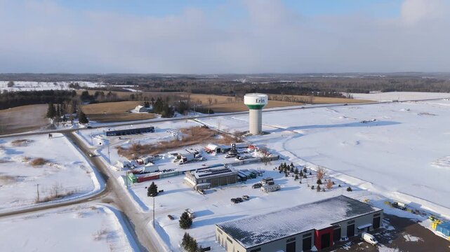Water Tower Surrounded By Industrial Business Buildings And Farm Fields During Winter. Drone Orbiting Shot.