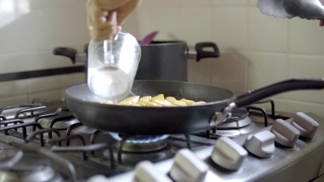 Hand adds ingredients to frying pan on stove for pollo al limon dish