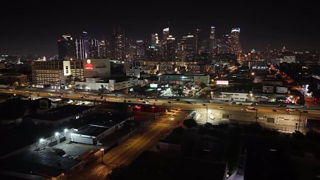 Cinematic aerial drone shot in Los Angeles at night, beginning across the 10 freeway and flying forward over moving traffic toward the illuminated downtown skyline.