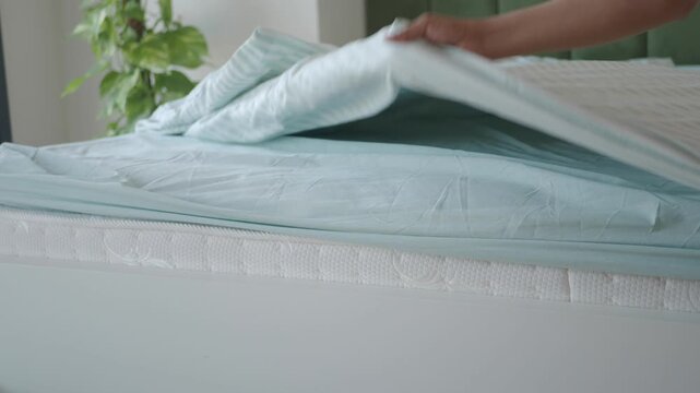 Hand smoothing blue bed sheet over white mattress and striped duvet.