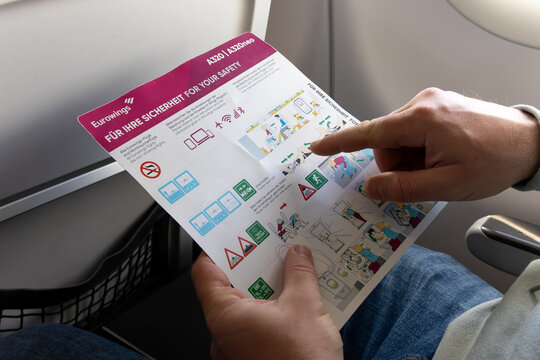 Funchal, Portugal - November 11, 2025: Passenger reading safety instruction card on an airplane, showing emergency procedures and safety symbols in a cabin setting