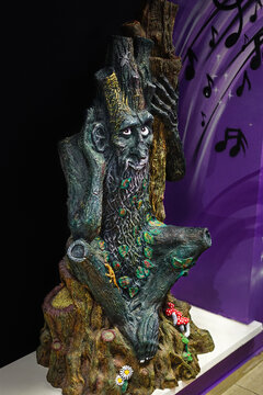 A fairytale sculpture of Leshy with a human face and a background of musical notes.
