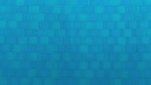 Underwater shot showing blue tiles of a swimming pool with clear water, showcasing the refreshing and clean atmosphere.
