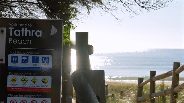 Tathra Beach sign with ocean and sunlight reflecting on water, Tathra, New South Wales, Australia.