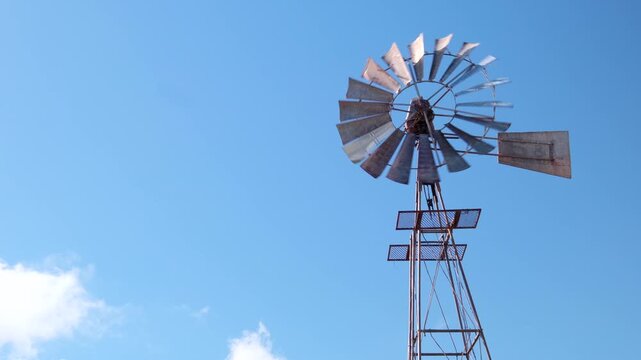 Windmill or windpump spinning in wind, upward view against blue sky