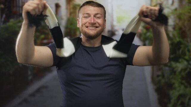 Man holding black and white scarf, arms raised and mouth open while shouting on a street; celebration victory support.