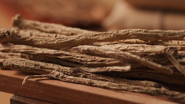 Rotating video of dried angelica root sticks arranged on a wooden tray. Close-up highlights elongated shapes, dry surface, and natural tones, representing traditional herbal medicine ingredients.