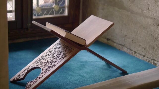 Open quran book on traditional wooden folding stand inside mosque with cinematic movement.