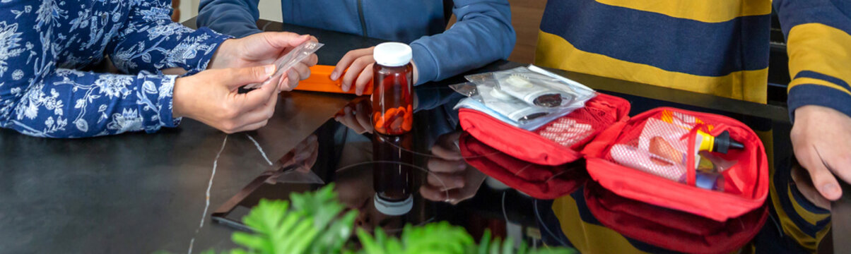 Banner of anonymous mother instructing two teenagers about medical supplies and first aid items, preparing them for health emergencies and personal care at home. Family preparing 72 hour survival kit.