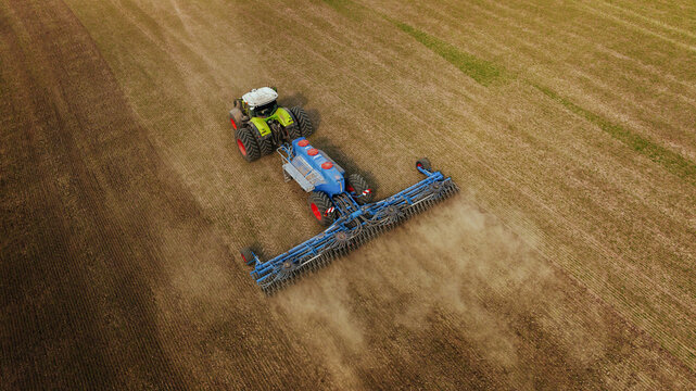 Agricultural tractor with attached tillage equipment working on a large field, dust rising from the soil, aerial view showcasing farmland and machinery in action