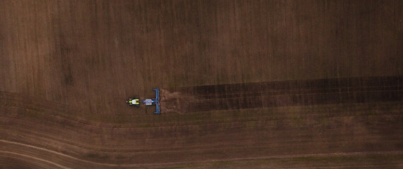 Aerial view of a tractor plowing a brown agricultural field with distinct soil patterns and tire tracks visible in the landscape © standret