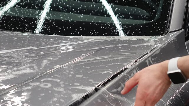 A car wrapping specialist applies a polyurethane film to the car. Detailer smoothes PPF. Car wrapping, detailing, tuning and styling. PPF protective film against chips and scratches. Car protection.