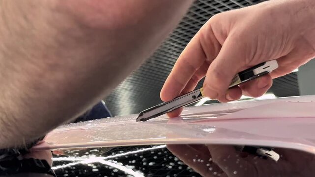 A car wrapping specialist applies a polyurethane film to the car. Detailer smoothes PPF. Car wrapping, detailing, tuning and styling. PPF protective film against chips and scratches. Car protection.