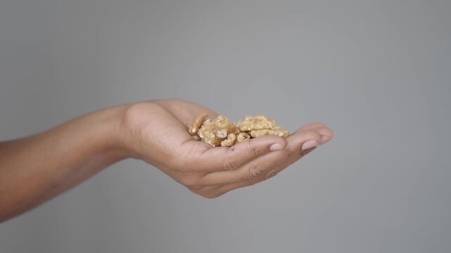 Person hand holding handful of organic walnut kernels against grey background studio shot.