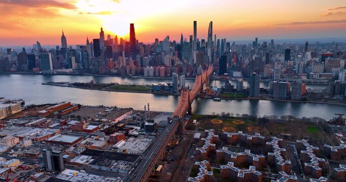 Approaching the Queensboro Bridge with cars heading to and from the structure. Aerial perspective on the stunning New York skyline against orange sky at sunset.