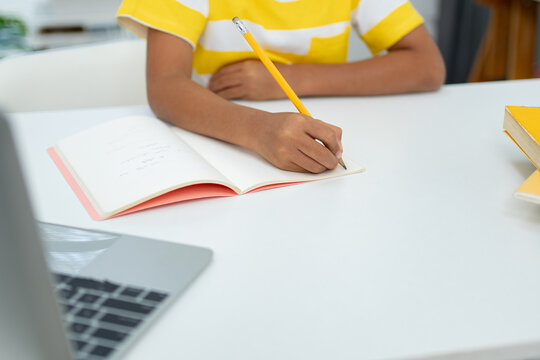 Child Writing Notes in Notebook with Laptop on Desk Online Learning