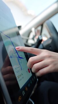 Woman's hand interacts with a modern car's touch screen navigation system for route planning. GPS map, destination, convenient driving technology concept. Vertical Shot
