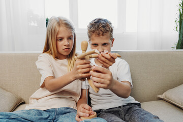 Boy and girl sitting on sofa play with wooden mannequin, focusing on creativity and imagination in...