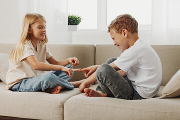 Happy young boy and girl sitting on beige sofa playing finger game in bright living room with natural light and casual clothes. © SHOTPRIME STUDIO