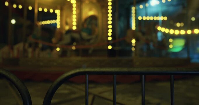 The atmosphere is serene as bright lights illuminate a deserted fairground carousel. Metal barriers are set up, hinting at evening entertainment that awaits visitors.