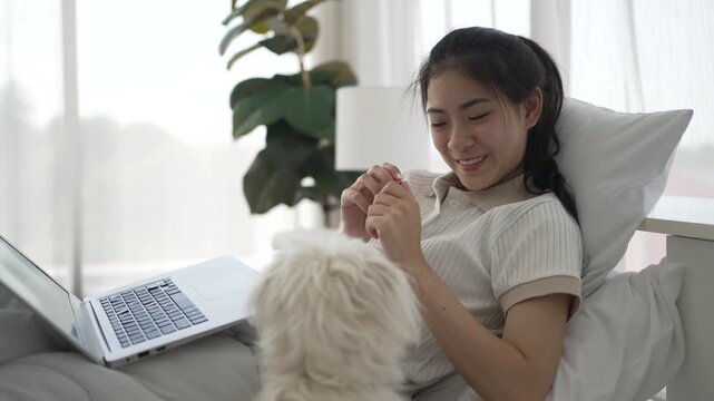 The Asian pretty woman is spending leisure time with her dog at the bedroom. Leisure activity, lifestyle, pet.