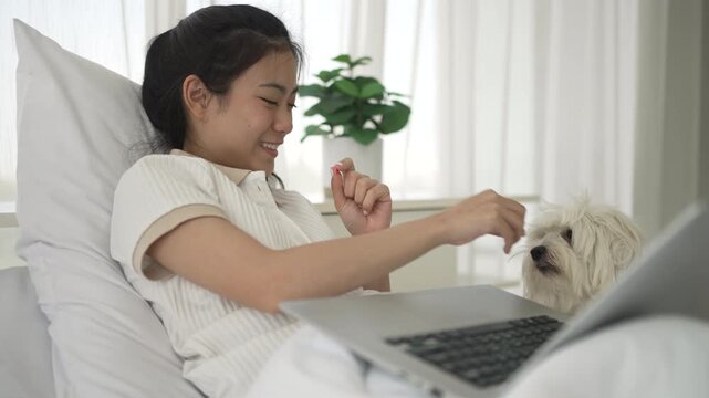 The Asian pretty woman is spending leisure time with her dog at the bedroom. Leisure activity, lifestyle, pet.