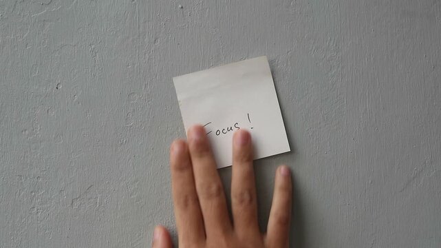 Hand sticking a post-it note with the word Focus! onto a textured grey wall