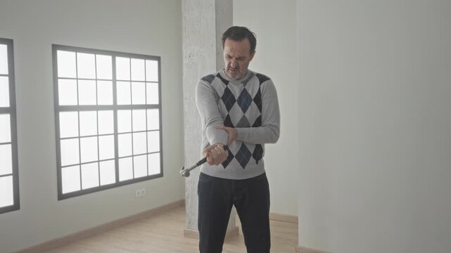 Man holding hammer and checking his wrist inside building after a mistimed strike, gripping the tool with a pained look; frustration.
