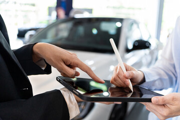 Close-up of Asian woman signing digital signature on tablet using a stylus in showroom. Successful...