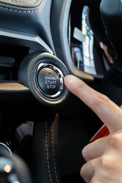 Modern automotive technology. A finger pushes the keyless start-stop button of a new vehicle. Vertical Shot