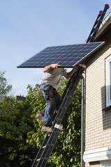 Man carrying a solar panel to a roof using a ladder in the Netherlands © Gertjan Hooijer