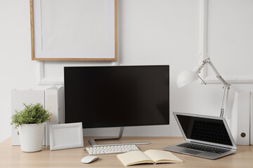 Fototapeta premium Workplace with blank computer monitor, laptop and lamp near light wall in office