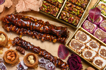 Assorted oriental sweets with kataifi nests, churchkhela, and turkish delight on craft paper. Traditional middle eastern dessert flat lay with walnuts and cinnamon on a wooden background.