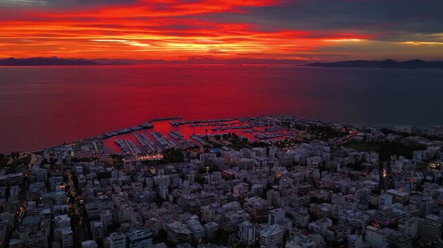 Aerial view of the coast of Athens, Greece, with Alimos district until Palio Faliro with public beaches and yacht marinas next to the illuminated skyline during a colorful sunset