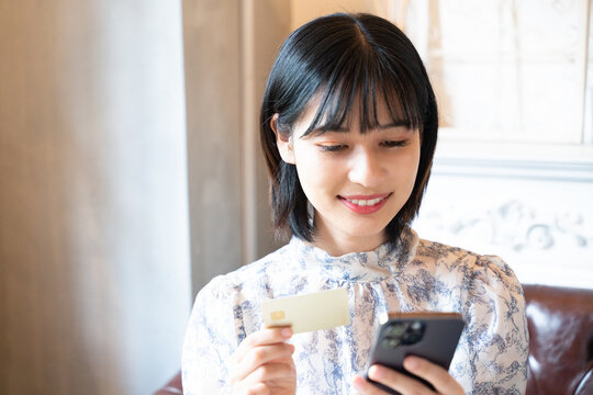 スマホを見ながらカードで決済をしようとしている女性