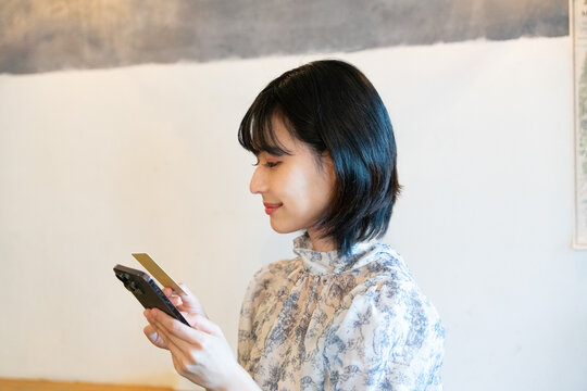 スマホを見ながらカードで決済をしようとしている女性