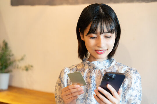 スマホを見ながらカードで決済をしようとしている女性