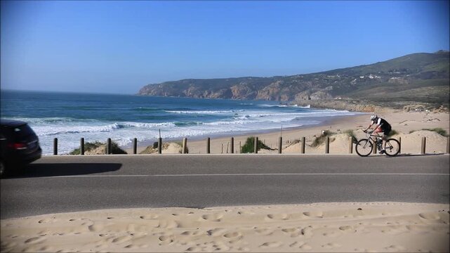 Scenic coastal road overlooking a sandy beach with rolling waves and distant cliffs