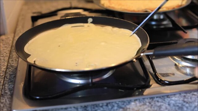 Cooking a thin crepe batter in a hot non-stick frying pan on the stove