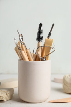 Holder with set of sculptor tools, clay and plaster figures on white table