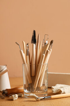 Holder with set of sculptor tools and clay on beige background